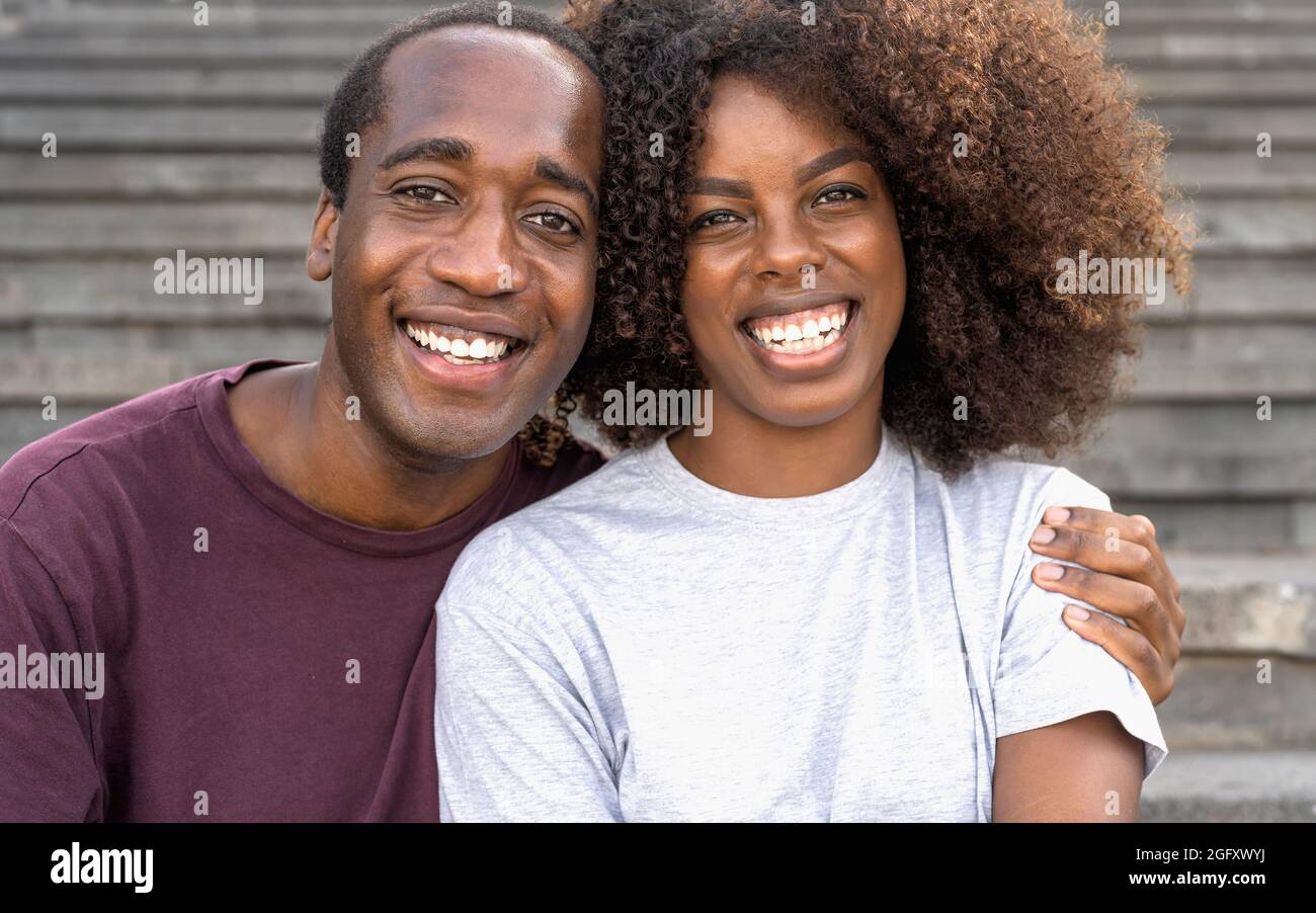 Glückliches afrikanisches Paar, das Spaß hat, in die Kamera zu lächeln, während es auf einer städtischen Treppe sitzt Stockfoto