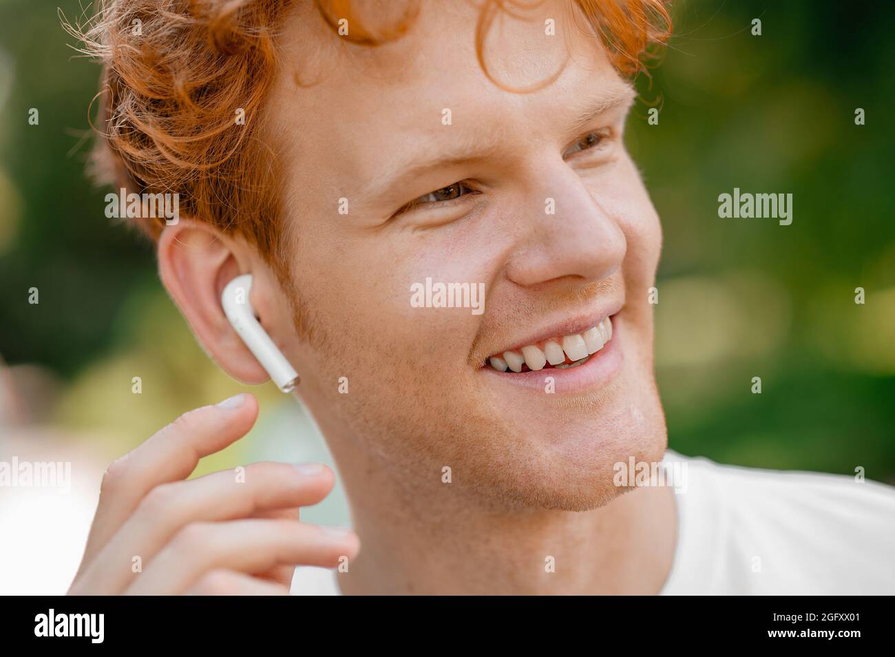 Ein fröhlicher Mann mit einem kabellosen Ohrstöpsel, der in die Ferne blickt Stockfoto