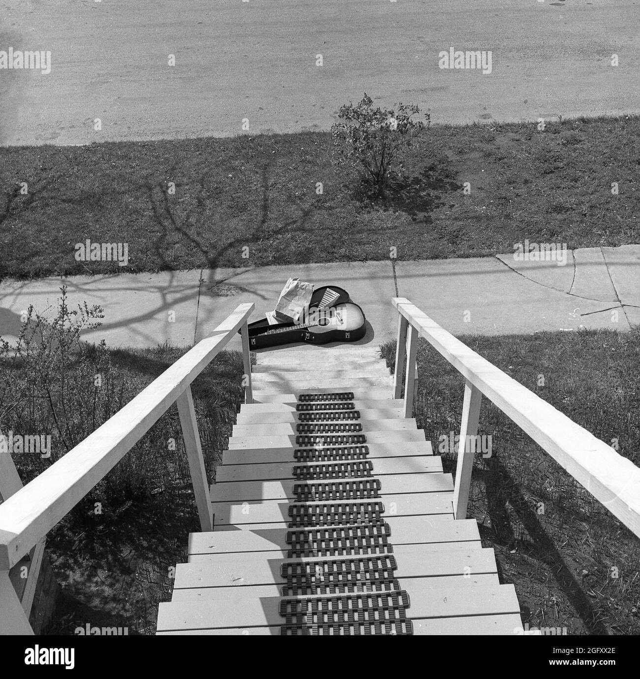 1950s, historial, eine akustische Gitarre, die in einem offenen Gehäuse mit Noten sitzt, auf einem Bürgersteig unten an einer Reihe von Holztreppen im Freien, USA. Stockfoto
