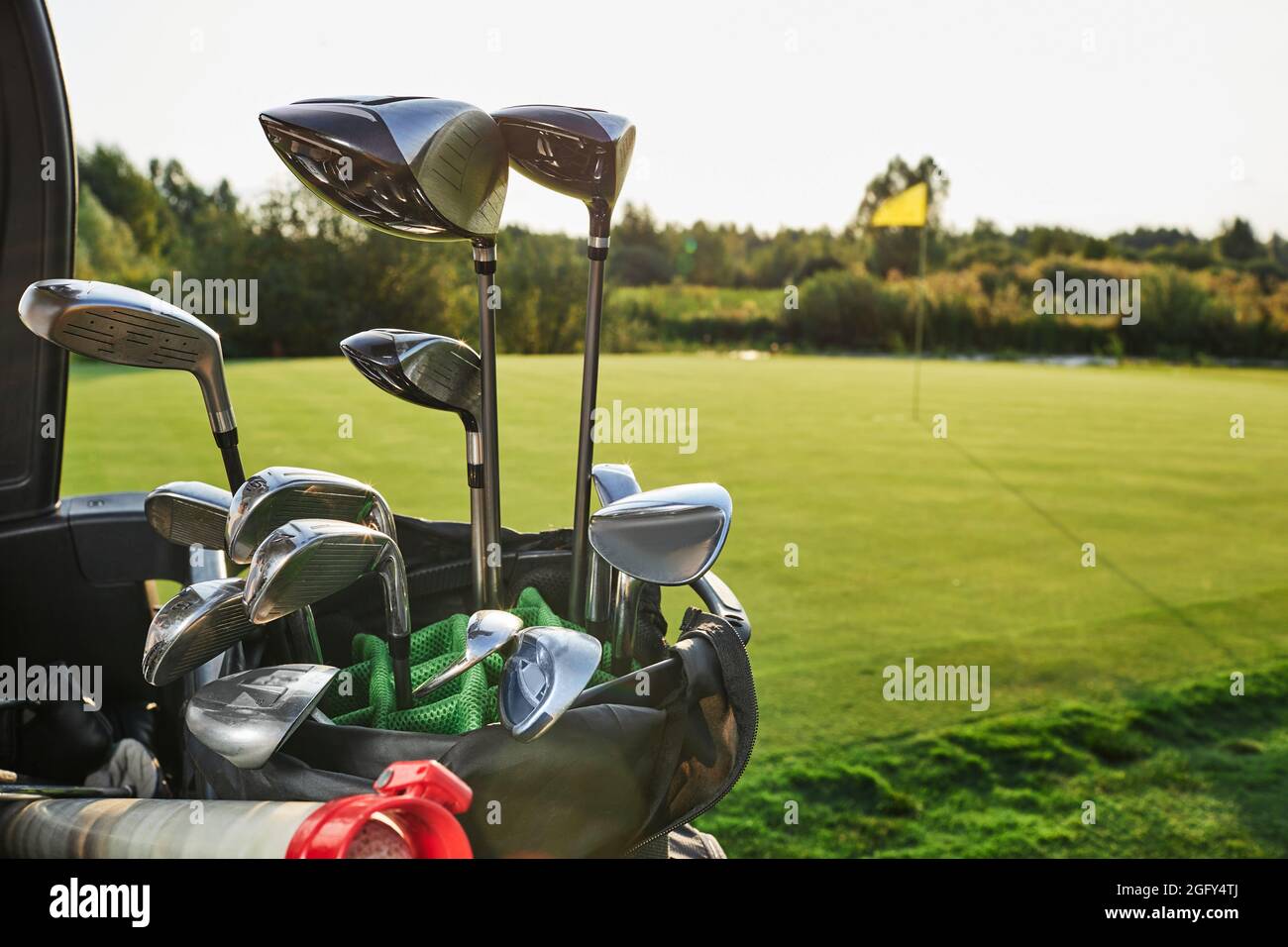 Metall-Golfschläger befinden sich in der Nähe, über dem Hintergrund eines Golfplatzes mit einem flagstick und einer wunderschönen Landschaft an einem sonnigen Tag Stockfoto