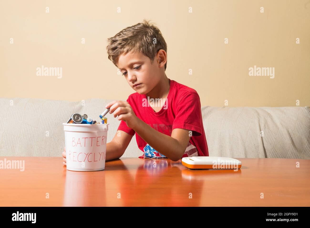 Ein Kind, das einen leeren Akku aus einem Spielzeug herausgenommen und in einen Recyclingbehälter gestellt hat. Konzept der Erziehung von Kindern in Umweltwerten. Stockfoto