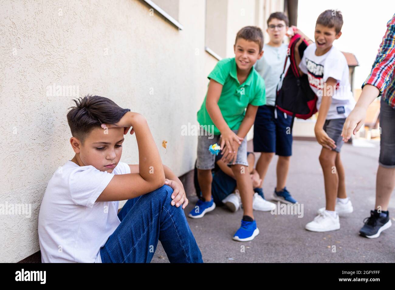 Eine Gruppe von Schuljungen schikaniert einen traurig und verärgert aussehenden Jungen. Stockfoto