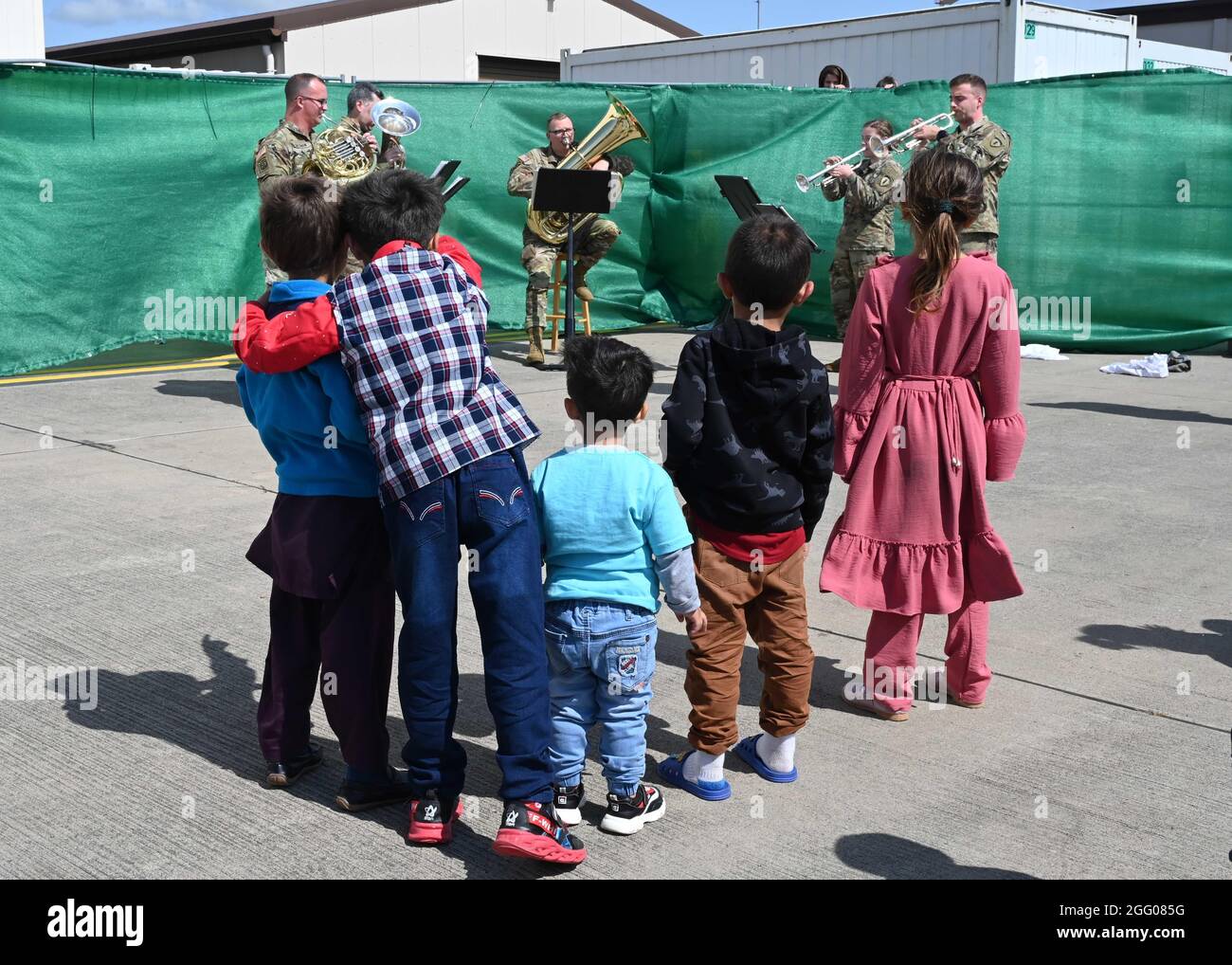 Ramstein Miesenbach, Deutschland. August 2021. Afghanische Kinder hören der U.S. Army Europe and Africa Band Musik, um Flüchtlinge auf dem Ramstein Air Base am 24. August 2021 in Ramstein-Miesenbach zu unterhalten. Der Luftwaffenstützpunkt Ramstein stellt im Rahmen der Operation Allies Refuge vorübergehend Unterkunft für Evakuierte aus Afghanistan bereit. Quelle: Planetpix/Alamy Live News Stockfoto