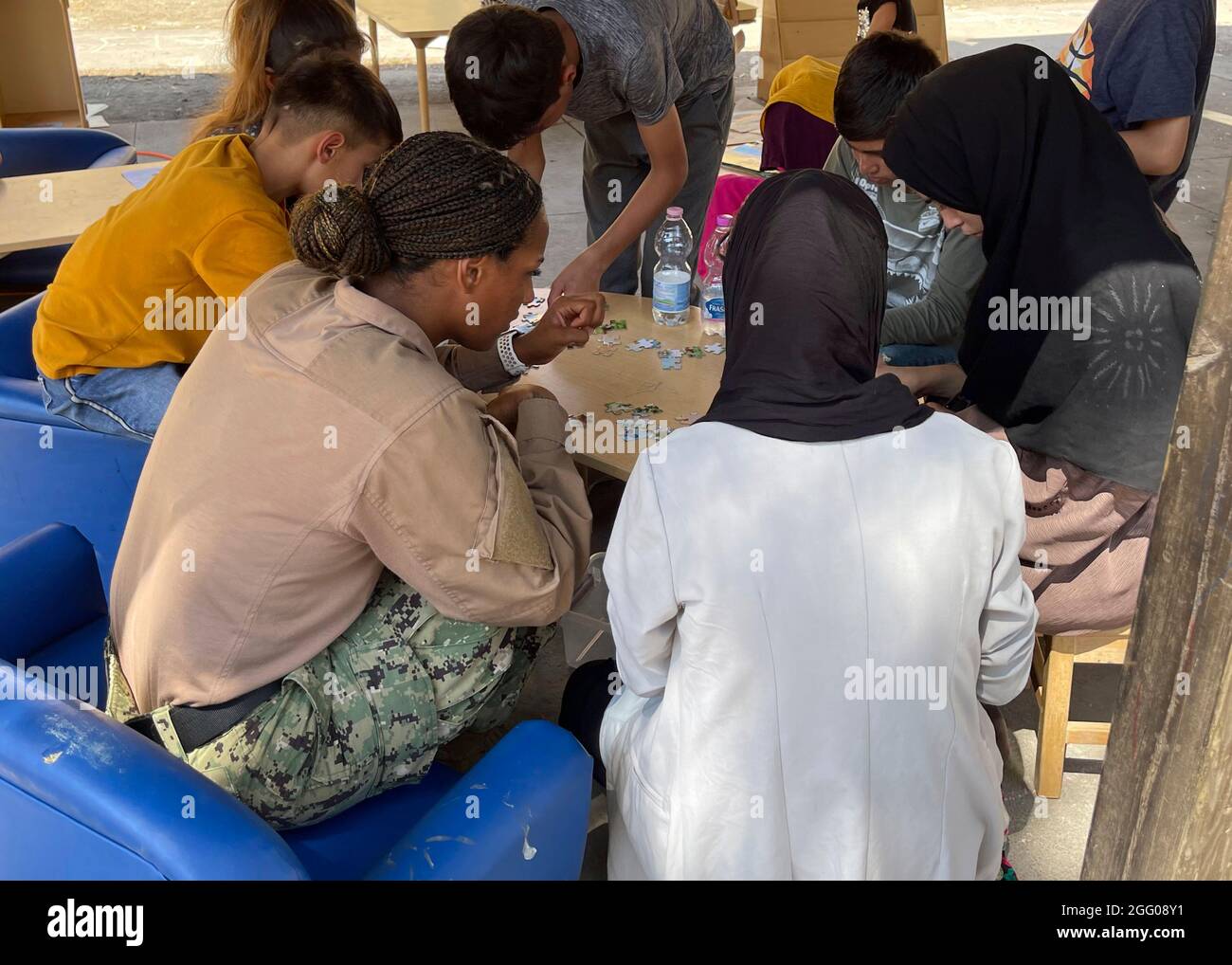 Sigonella, Italien. August 2021. Ein Seemann der US-Marine und afghanische Evakuierte montieren am 24. August 2021 in Sigonella, Italien, ein Puzzle auf der Naval Air Station Sigonella. NAS Sigonella stellt im Rahmen der Operation Allies Refuge eine vorübergehende Unterkunft für Evakuierte aus Afghanistan bereit. Quelle: Planetpix/Alamy Live News Stockfoto