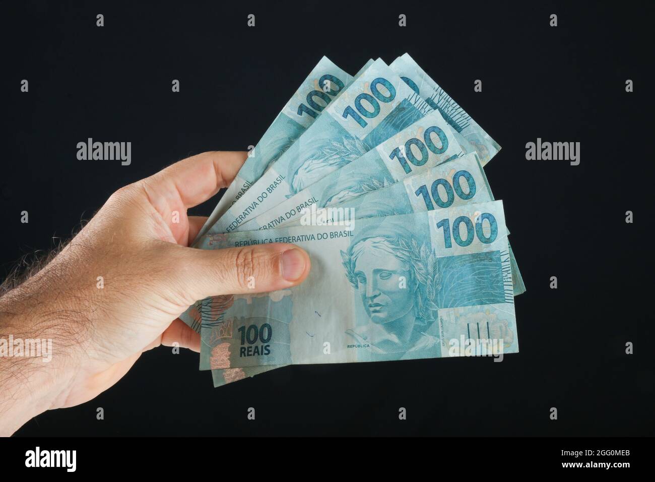 Hand hält brasilianisches Geld. 100-reais-Banknoten. Schwarzer Hintergrund. Stockfoto