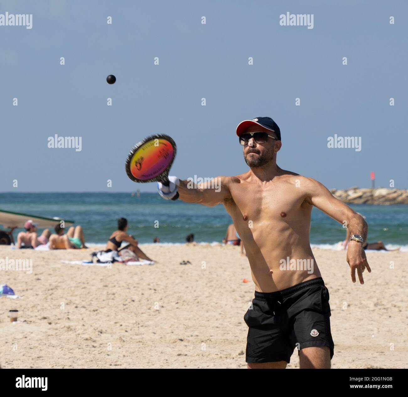 Tel Aviv, Israel - 15. August 2021: Ein junger Mann während eines matkot-Spiels am Strand von Tel Aviv, Israel, an einem klaren, sonnigen Tag. Stockfoto