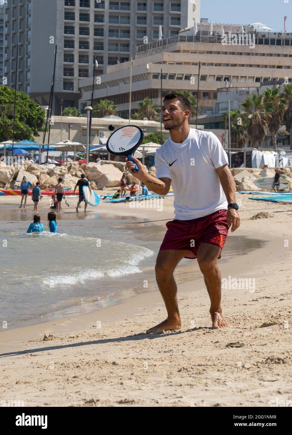 Tel Aviv, Israel - 15. August 2021: Ein junger Mann während eines matkot-Spiels am Strand von Tel Aviv, Israel, an einem klaren, sonnigen Tag. Stockfoto