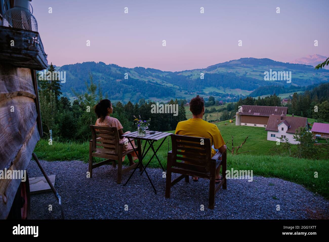 Schweiz Countryside, Ebnat Kappel, Sankt-Gallen, Schweiz, Paar Mann und Frau blicken auf den Sonnenuntergang vor ihrer blechenden Hütte über den Wiesen der Schweiz. Stockfoto