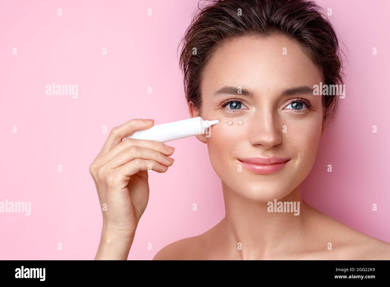 Schöne Frau mit Creme um die Augen. Foto von Frau mit perfektem Make-up auf rosa Hintergrund. Schönheits- und Hautpflegekonzept Stockfoto