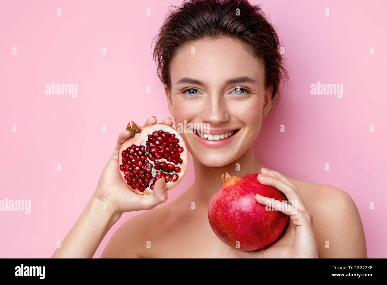 Lachende junge Frau mit Granatäpfeln. Foto von attraktiven Frau mit perfektem Make-up auf rosa Hintergrund. Beauty & Hautpflege Konzept Stockfoto