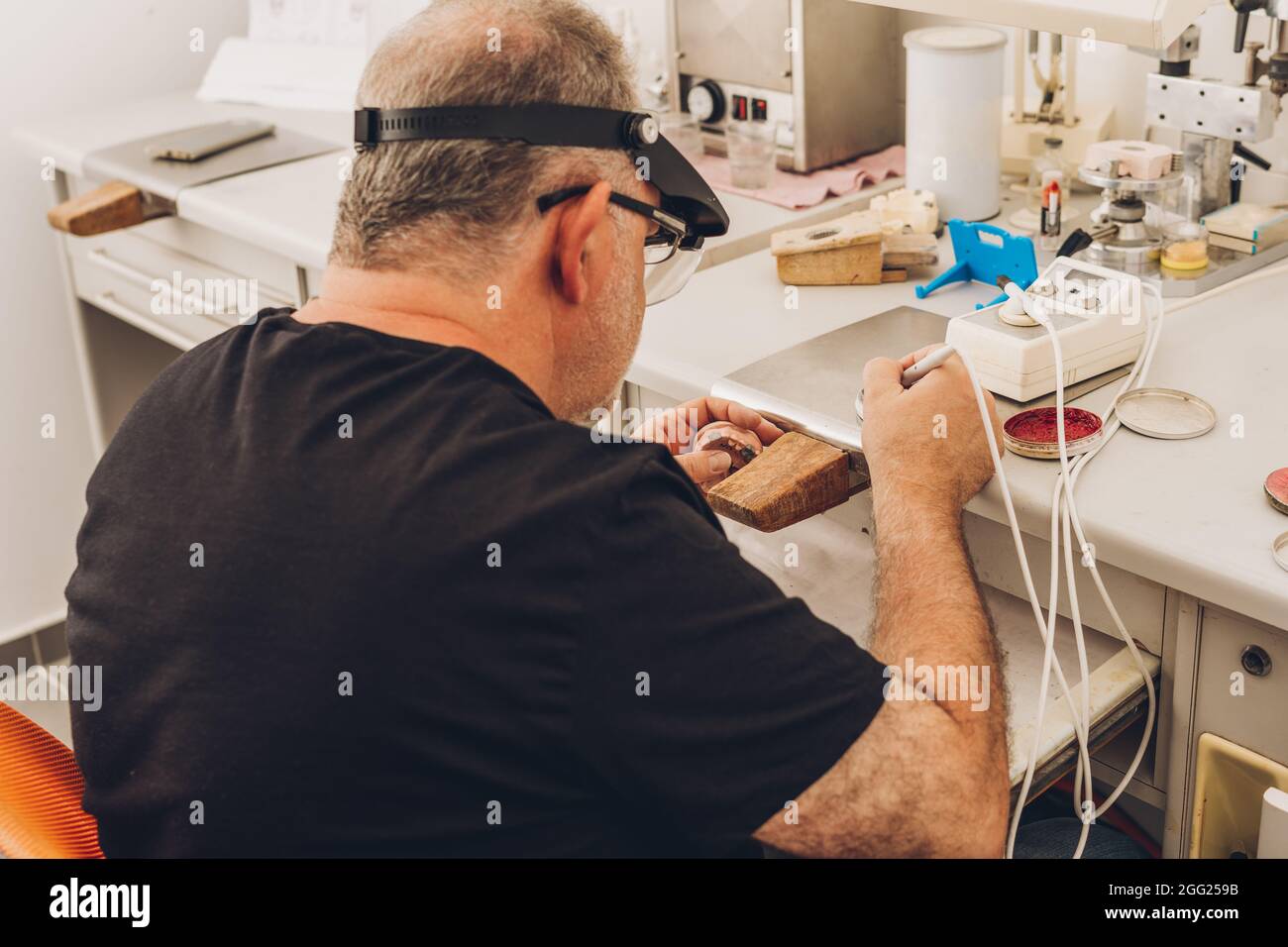 Mann, der in einem Zahnlabor sitzt, das sich auf professionelle Knochenzahnheilkunde spezialisiert hat und Wachs verwendet, um eine Zahnform zu Formen Stockfoto