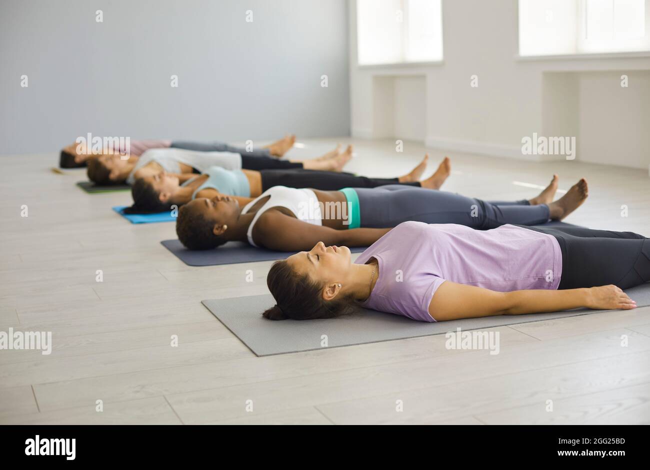 Verschiedene Frauen, die auf einer Matte liegen, meditieren im Fitnessclub Stockfoto