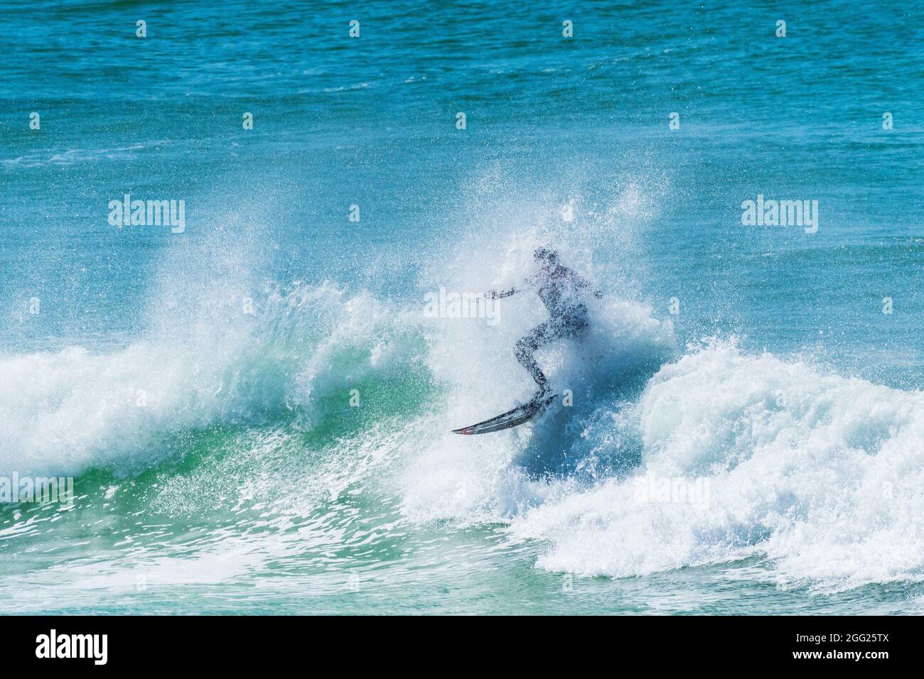 Spektakuläre Surfaktionen als Surfer werden von Spray überfluten, während er auf einer Welle im Fistral in Newquay in Cornwall reitet. Stockfoto
