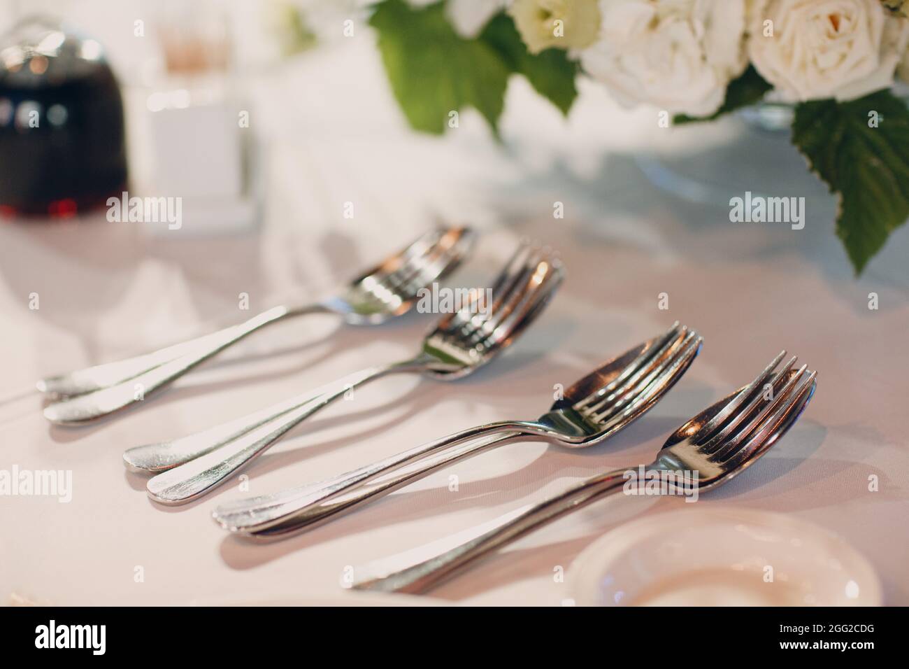 Runde Tische im Restaurant mit weißen Tischdecken und weißen Blumensträußen mit Löffel und Gabel. Stockfoto
