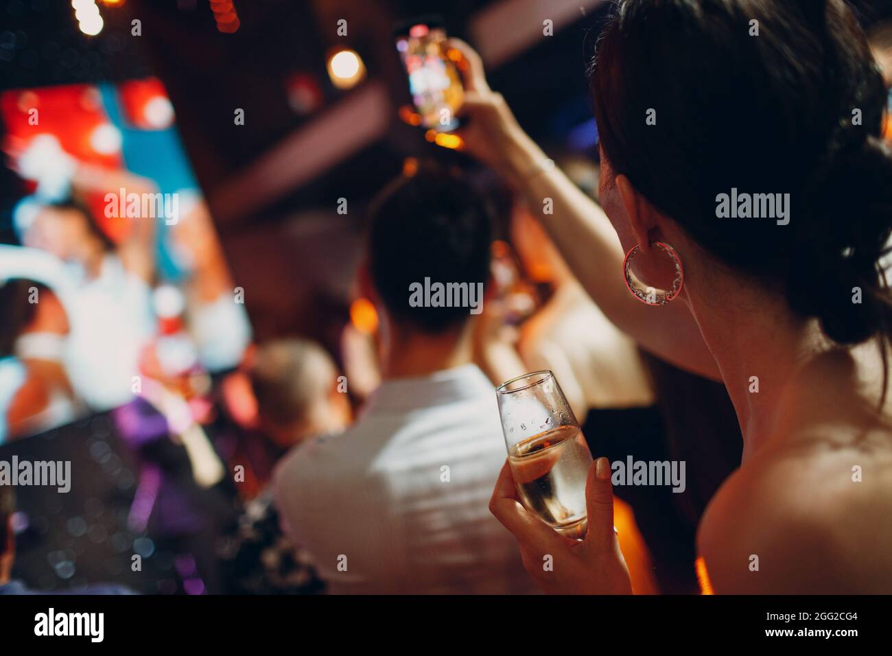 Rückansicht Frau mit Mobiltelefon und beschmiß gekühltes Glas Champagner auf der Party in der Hand. Stockfoto