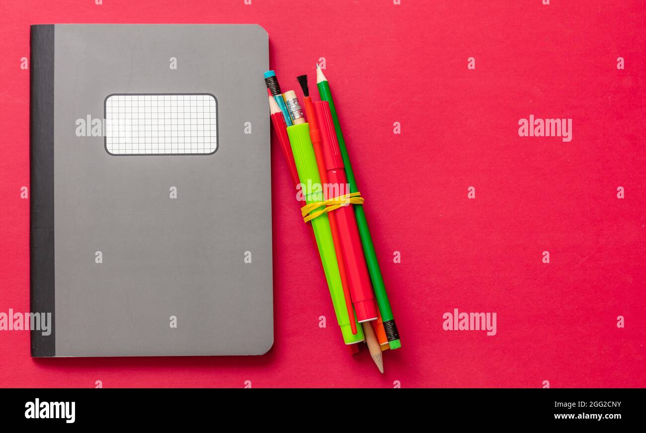 Schulbedarf, graues Notizbuch und Bleistifte auf rotem Hintergrund, Draufsicht, Kopierraum, Vorlage. Bildung, Back to School, Kreativität der Kinder Stockfoto