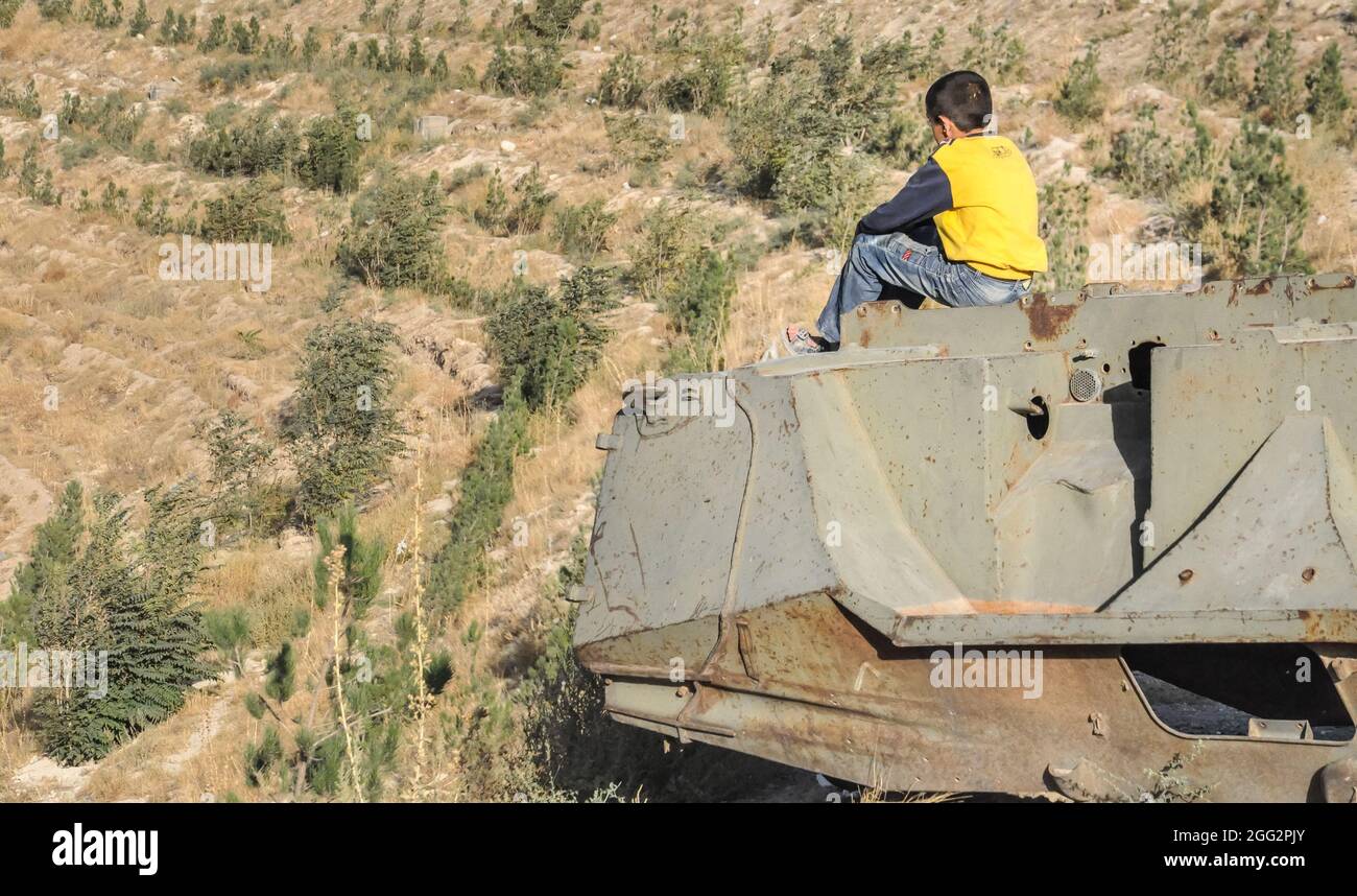 Junge sitzt auf zerstörten Tank auf den Hügeln über Kabul City in Afghanistan Stockfoto