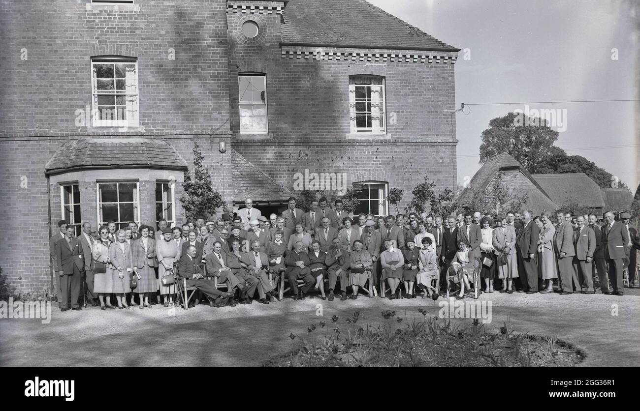 In den 1950er Jahren, historisch, in der formellen Kleidung der Ära, versammelt sich eine große Gruppe von Menschen, die an einer Konferenz teilnehmen, um vor einem Landhaus, Witney, Oxford, England, Großbritannien, ein Foto zu machen. Stockfoto