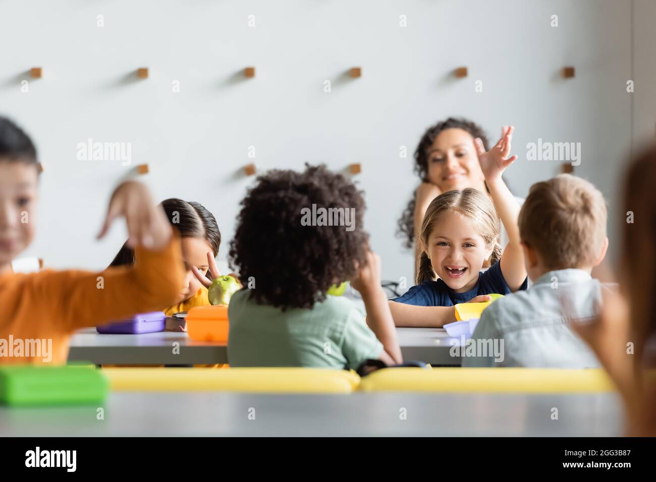Aufgeregte multiethnische Kinder winken beim Mittagessen in der Schulkantine mit den Händen Stockfoto