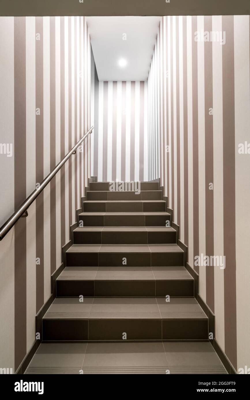 Vertikale Aufnahme einer dunkel beleuchteten Treppe mit vertikalen dunklen und weißen Streifen an den Wänden. Konzept für Labyrinth, Labyrinth, Geheimnis, geheime Kammer. Stockfoto