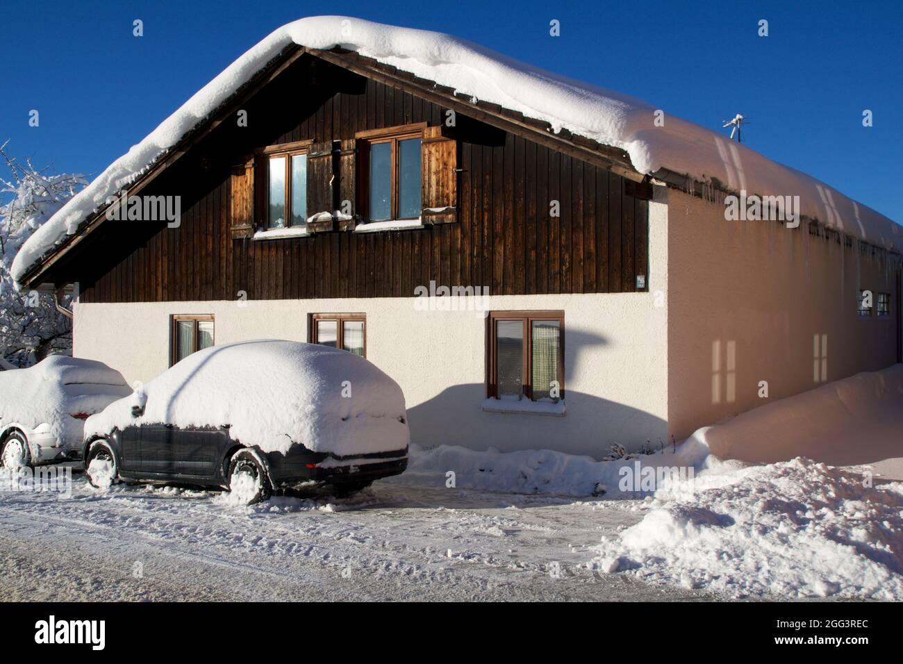 OBERSTAUFEN, DEUTSCHLAND - 29 DEZ, 2017: Typisches Holzhaus in den deutschen Alpen im Winter mit viel Schnee auf dem Dach und einem schneebedeckten Auto davor Stockfoto