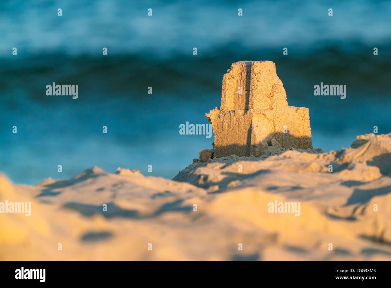 Ein kleiner Sandburgenturm, der am frühen Sommermorgen an einem Strand mit blauer Flut im unscharfen Hintergrund errichtet wurde. Spaß an der Ostseeküste in Hel Stockfoto
