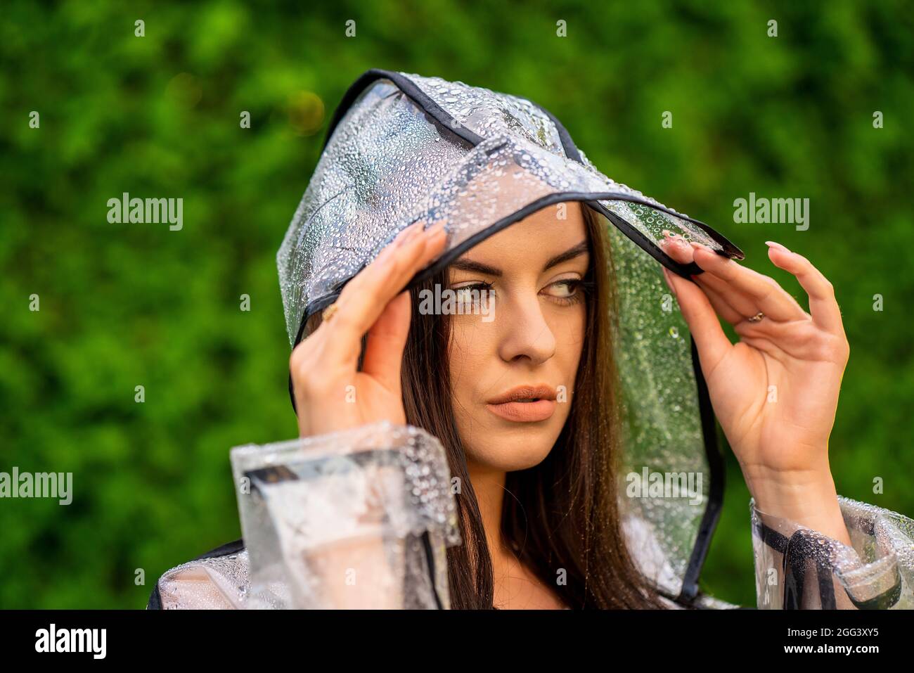 Junge schöne Frau im Regenmantel mit Kapuze an regnerischen Tagen Stockfoto