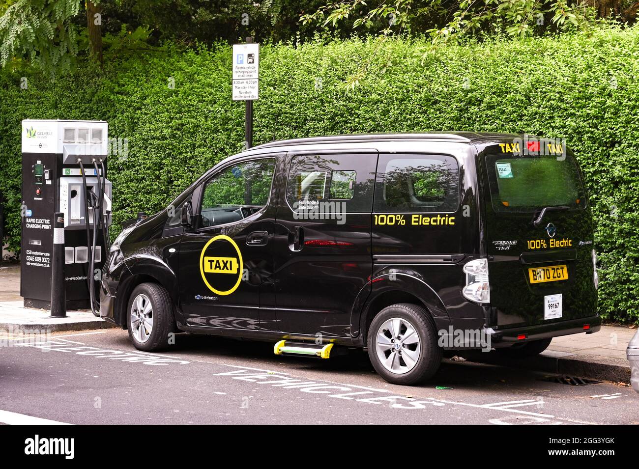 London, England - August 2021: London Taxi voll mit Strom betrieben, verbunden mit einer elektrischen Ladestation auf einer Stadtstraße. Stockfoto