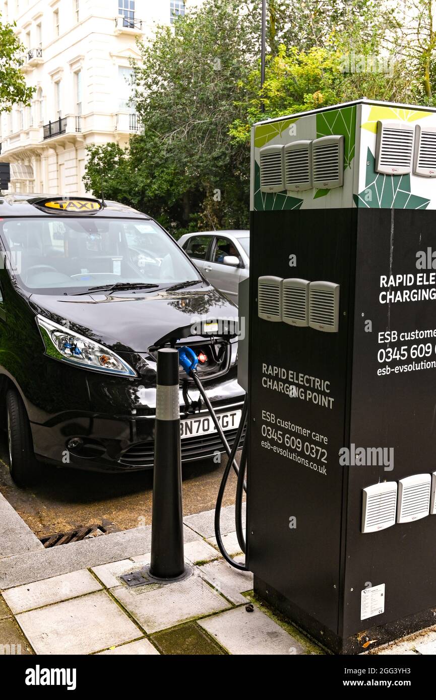 London, England - August 2021: London Taxi voll mit Strom betrieben, verbunden mit einer elektrischen Ladestation auf einer Stadtstraße. Stockfoto