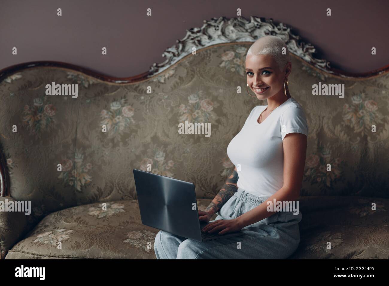 Eine junge Frau aus Europa mit einer kurzen blonden Frisur, die mit einem Laptop sitzt und lächelt. Arbeiten am freiberuflichen Konzept des Heimbüros. Stockfoto