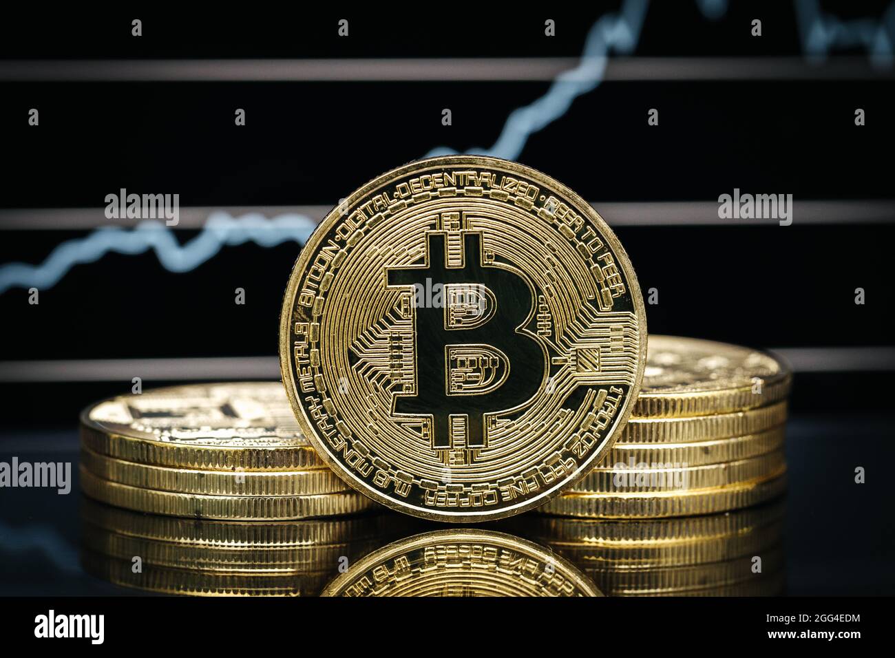 Bitcoin physische Münze aus der Nähe, vor einem Kursdiagramm Stockfoto