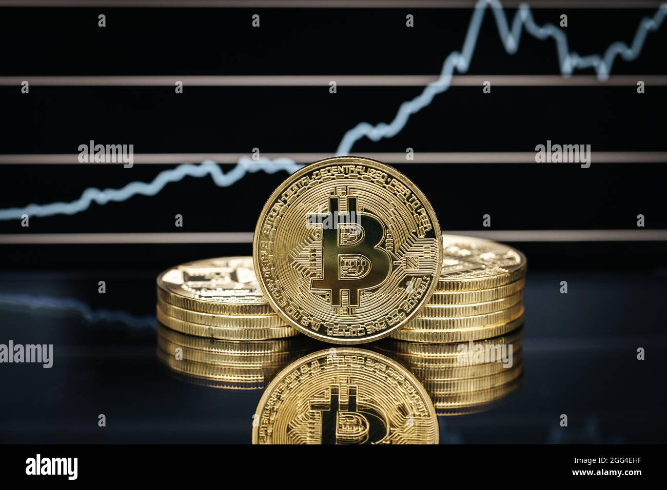 Bitcoin physische Münze aus der Nähe, vor einem Kursdiagramm Stockfoto