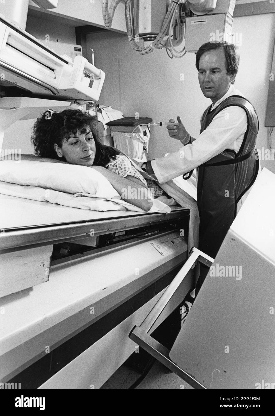 Austin Texas USA, um 1992: Radiologin mit Bleischutzweste bereitet weibliche Patientin auf die myelogramsichen Untersuchungen des Rückenmarks und der Nerven vor. ©Bob Daemmrich Stockfoto