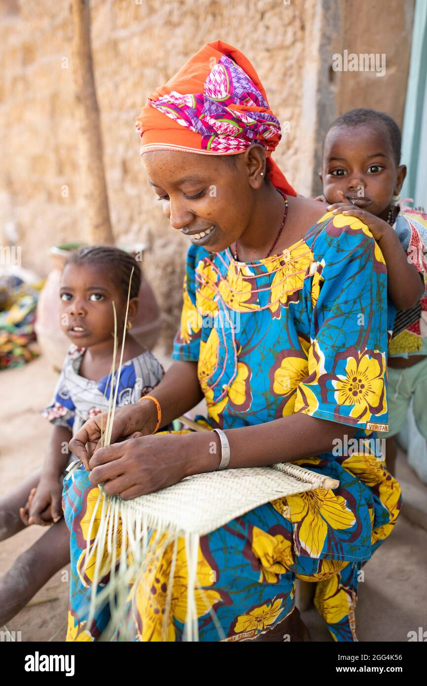 Eine Fulani-Mutter webt Matten und Fans von Hand aus getrockneten Palmwedeln für den Lebensunterhalt ihrer Familie in der Region Ségou, Mali, Westafrika. Stockfoto