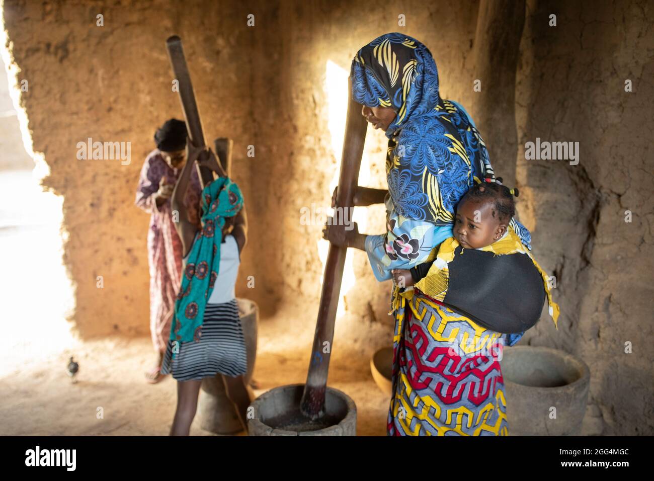 In der Region Ségou, Mali, Westafrika, arbeiten afrikanische Frauen und Mädchen zusammen, um mit traditionellen Holzmörteln und Stößeln Getreide in Mehl zu hämmern. Stockfoto