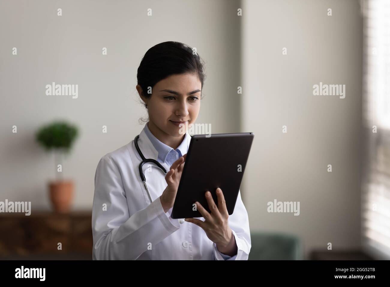 Konzentrierte junge indische Ärztin mit digitaler Tablette. Stockfoto