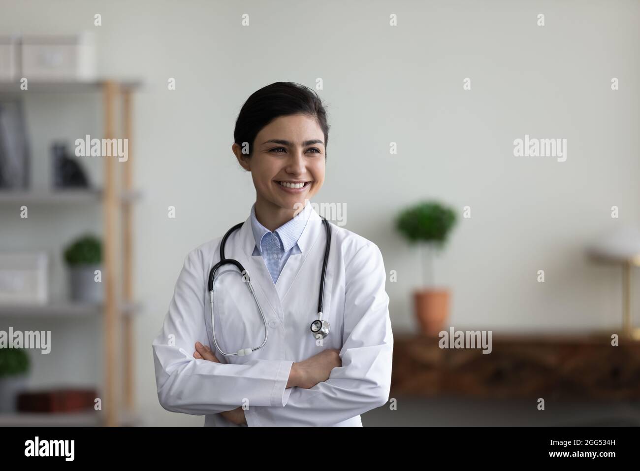 Selbstbewusste glückliche junge indische Ärztin, die drinnen steht. Stockfoto