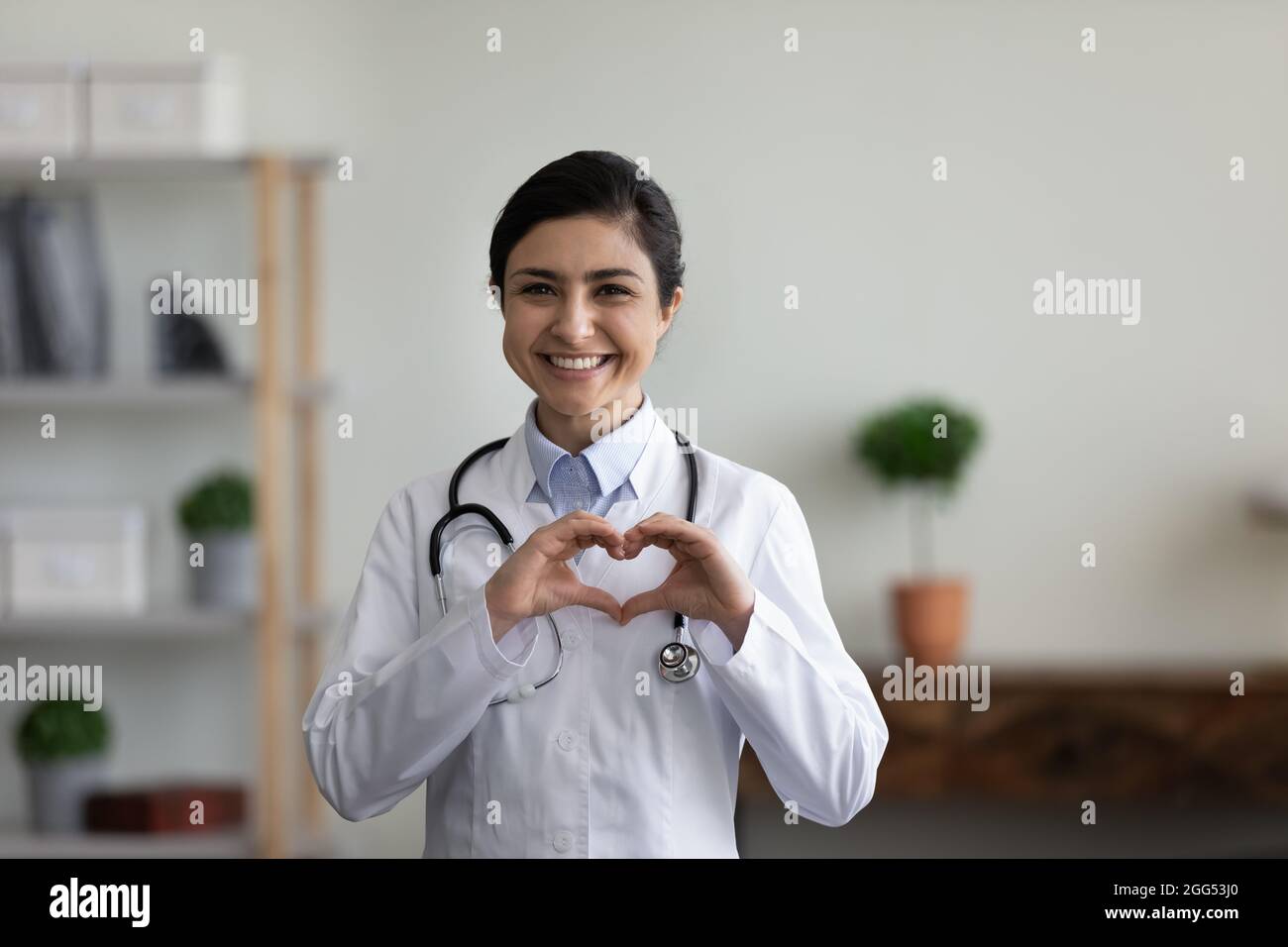 Lächelnd schöner junger indischer Arzt, der ein Liebessymbol zeigt. Stockfoto