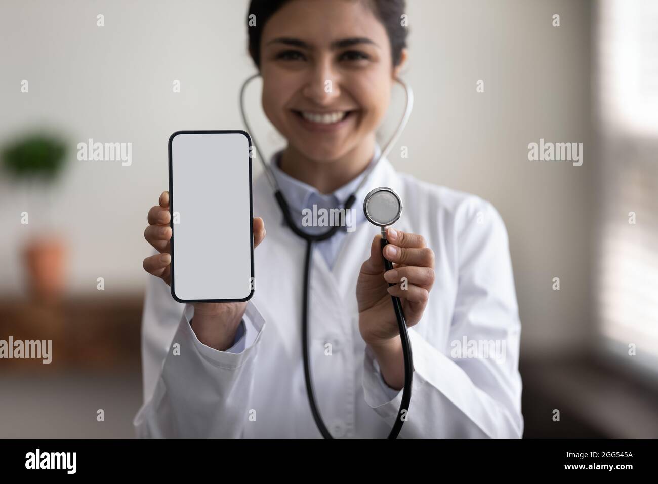 Nahaufnahme einer jungen indischen Kardiologin mit Mobiltelefon und Stethoskop. Stockfoto