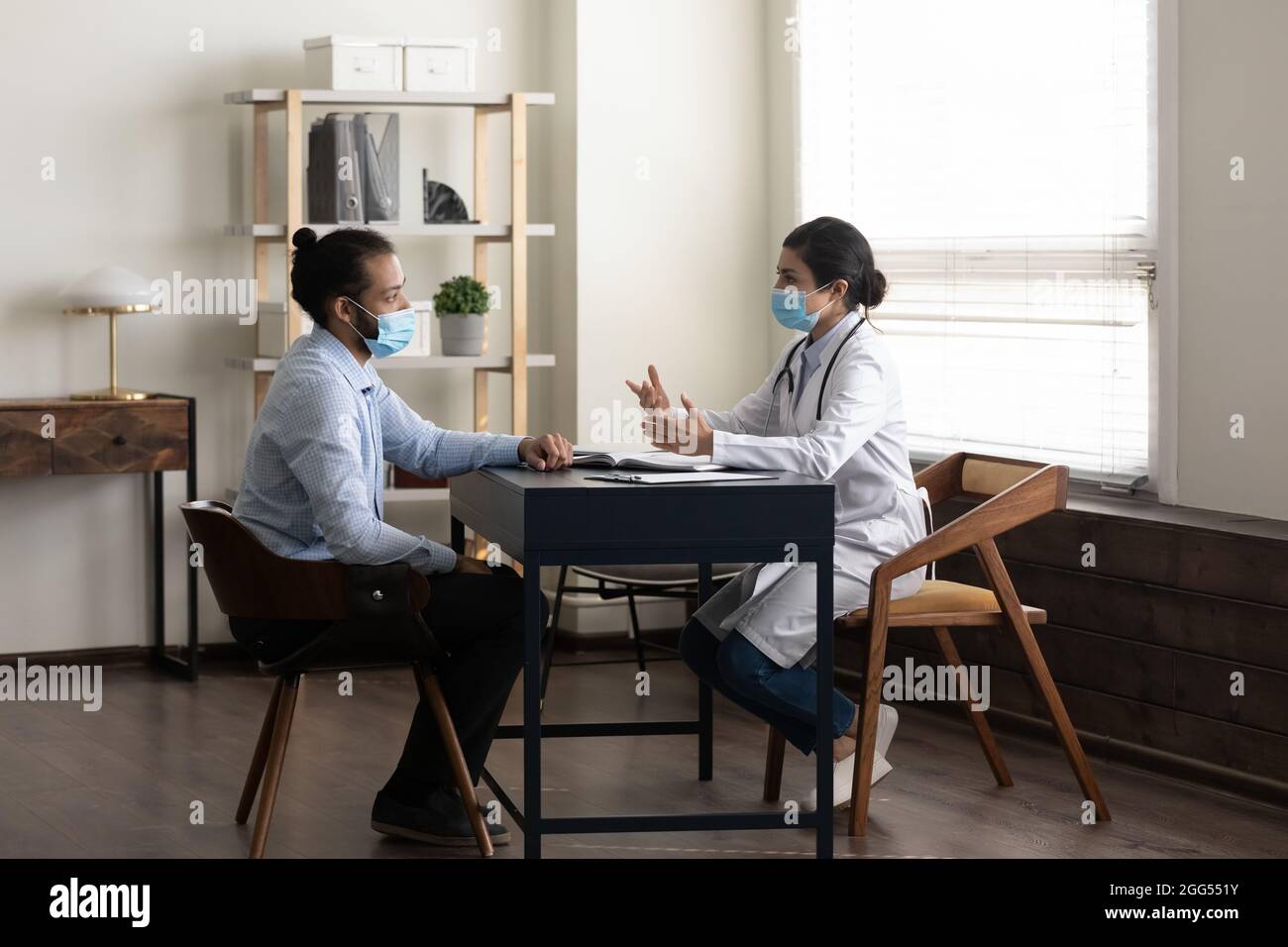 Konzentrierter junger afrikanischer Patient im Gespräch mit einem indischen Arzt. Stockfoto