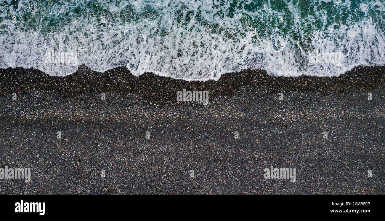 Meereswellen brechen am schwarzen Sandstrand, Meereshintergrund aus der Luft Stockfoto