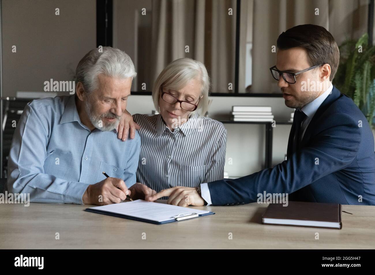 Reifes Paar, das Vertrag unterzeichnet und sich mit dem Manager im Büro abfindet Stockfoto