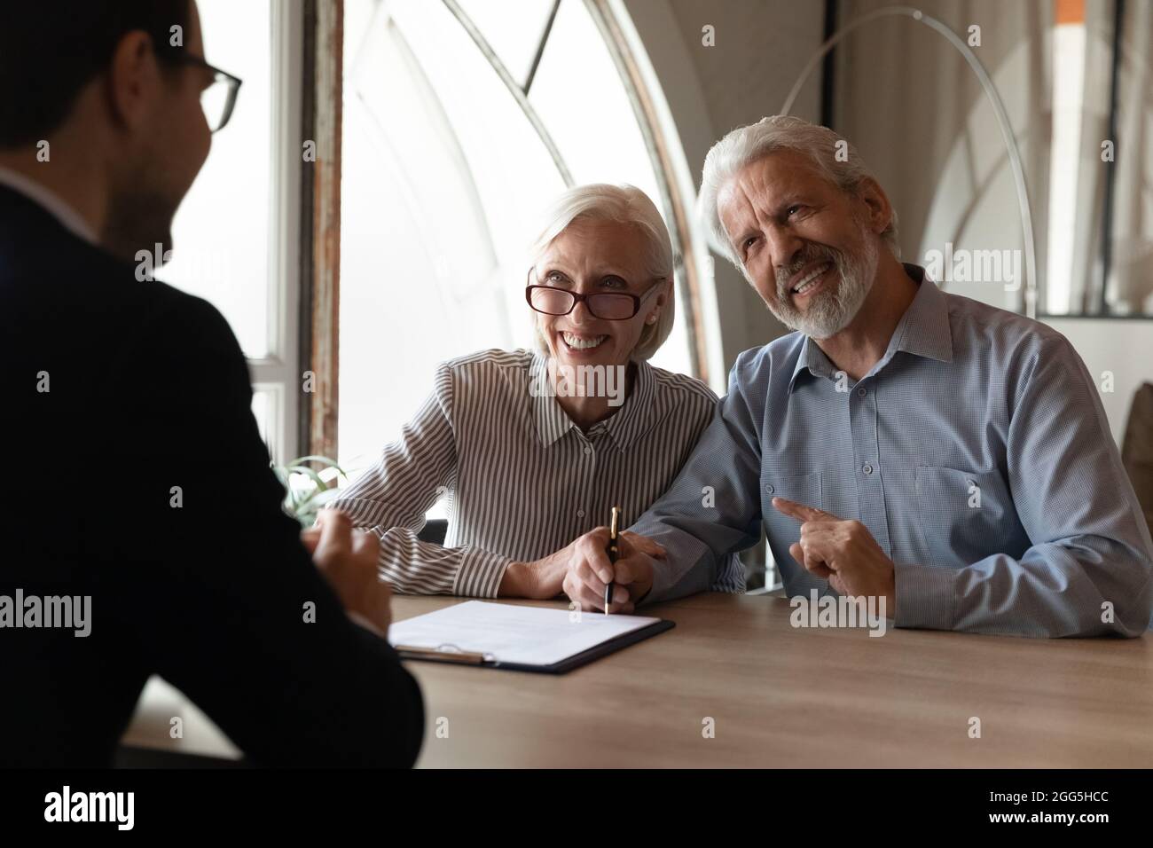Aufgeregt reifes Paar, das beim Treffen mit dem Manager eine Vereinbarung unterzeichnet hat Stockfoto