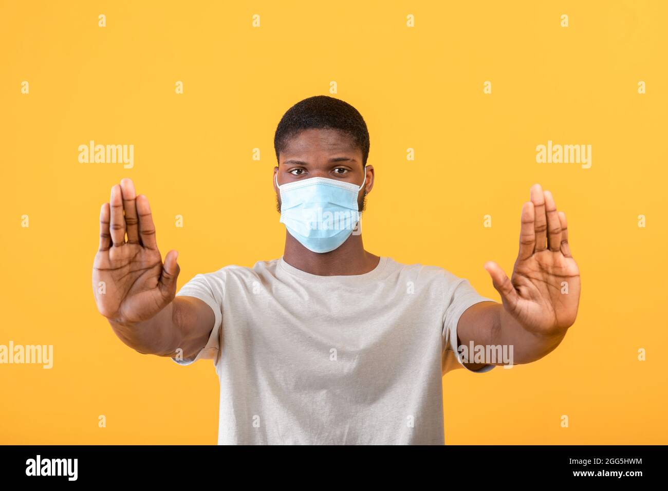 afroamerikanischer Mann in Gesichtsmaske, der zum STILLSTAND kommt und Negativität gegenüber einer Coronavirus-Pandemie ausdrückt Stockfoto