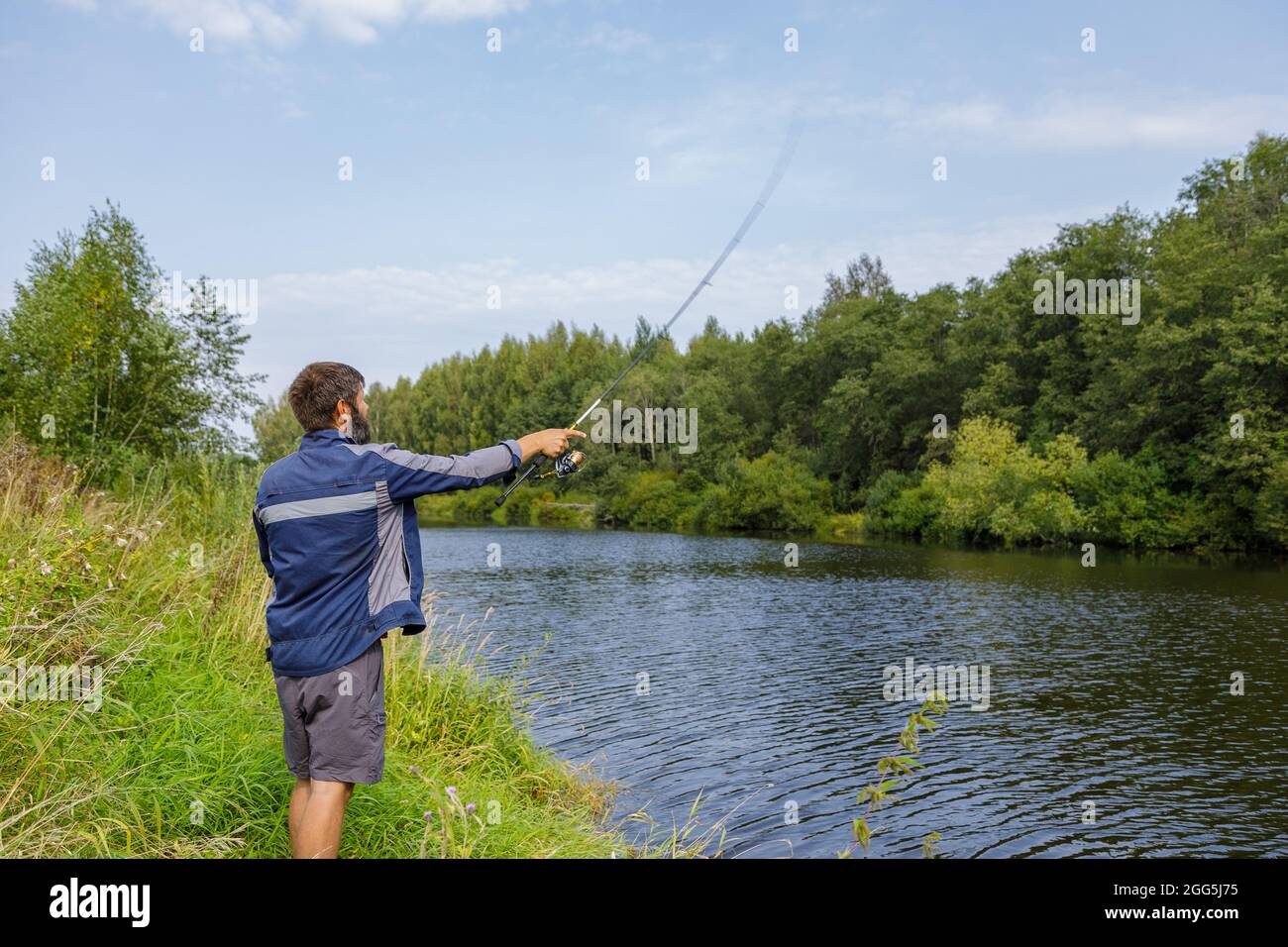 Ein Mann mit Bart fischt auf dem Fluss und wirft eine Leine. Ein Fischer mit einer Angelrute fischt am Flussufer. Stockfoto