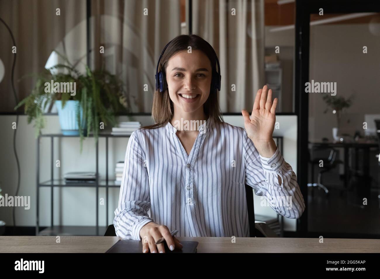 Porträt lächelnde Geschäftsfrau in Kopfhörer winkende Hand Stockfoto