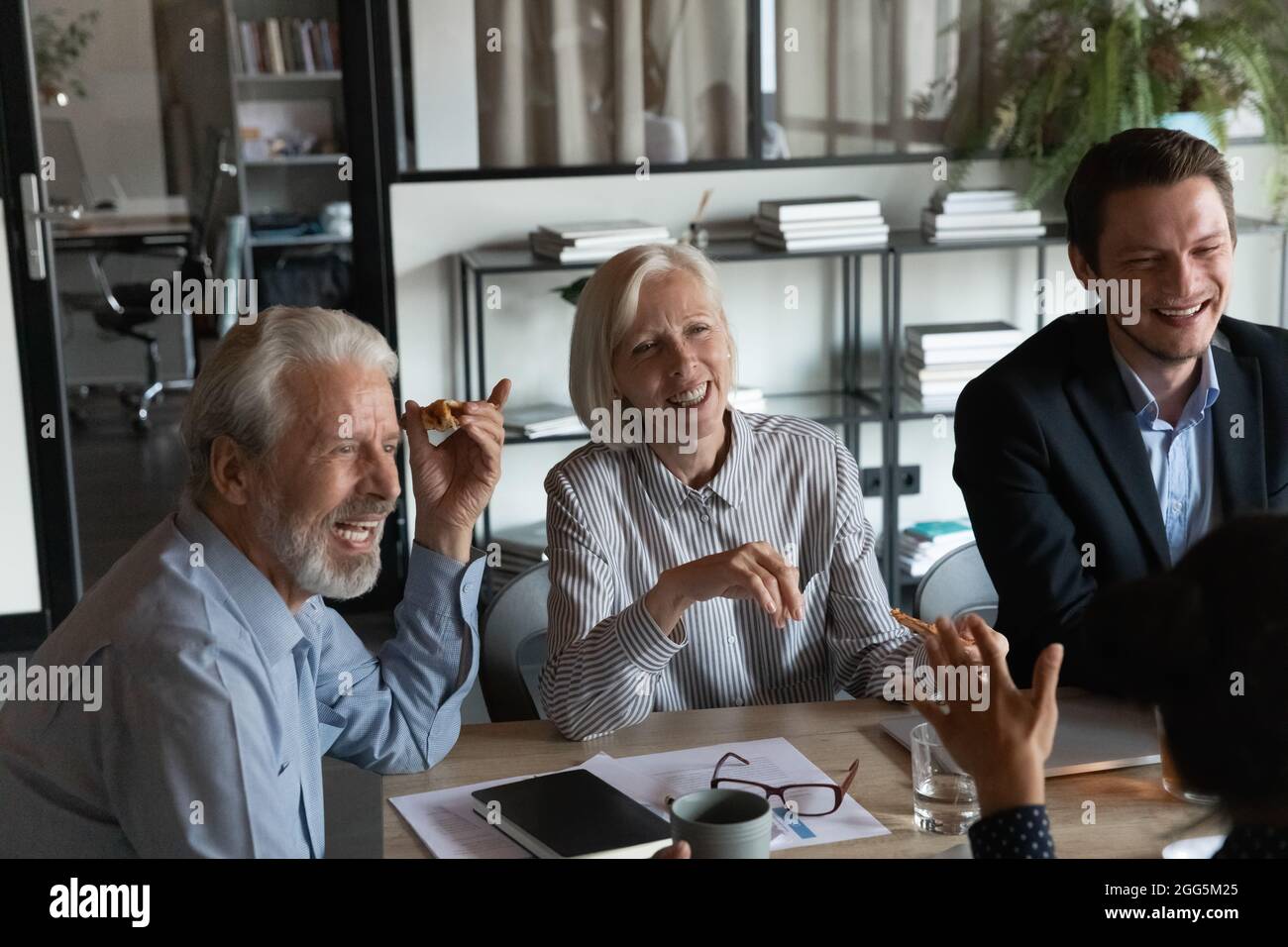 Aufgeregte, reife Geschäftsleute, die in den Pausen gemeinsam Pizza essen Stockfoto