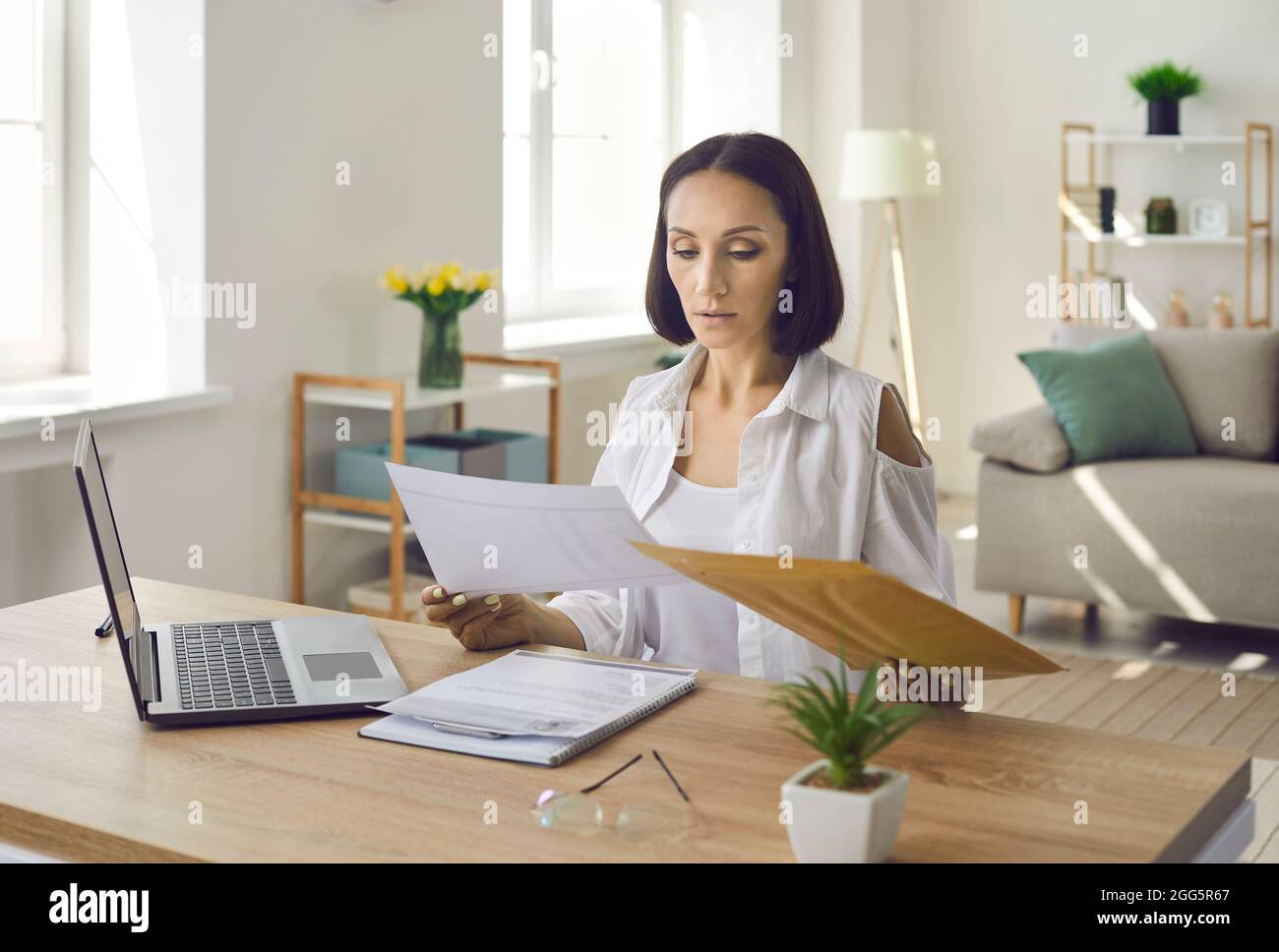 Frau, die in ihrem Heimbüro am Schreibtisch sitzt und Geschäftsbriefe und Dokumente liest Stockfoto