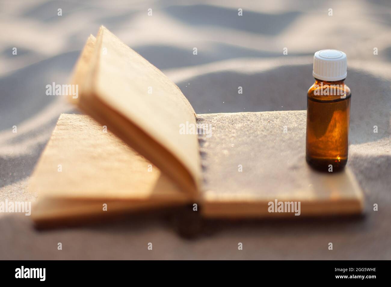 Flasche mit Ölextrakt auf Sand, und öffnen Sie das Buch. Platz für Text kopieren. Alternativmedizin, Rezept. Stockfoto