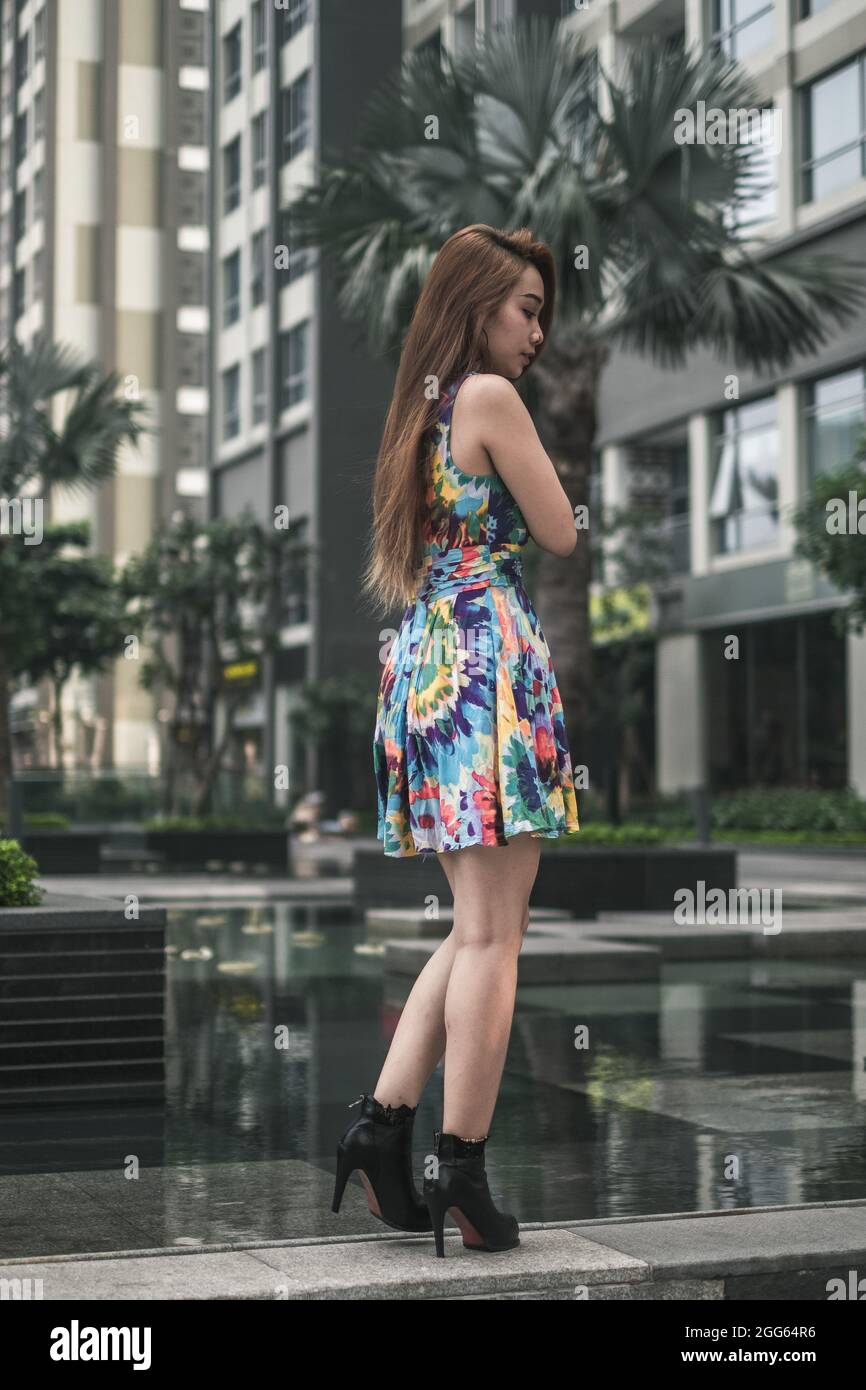 Schöne asiatische Frau in lässigen bunten Kleid steht im Freien in der Nähe des modernen Gebäudes. Langes Haar. Schöne Haltung. Hochwertige Fotos Stockfoto